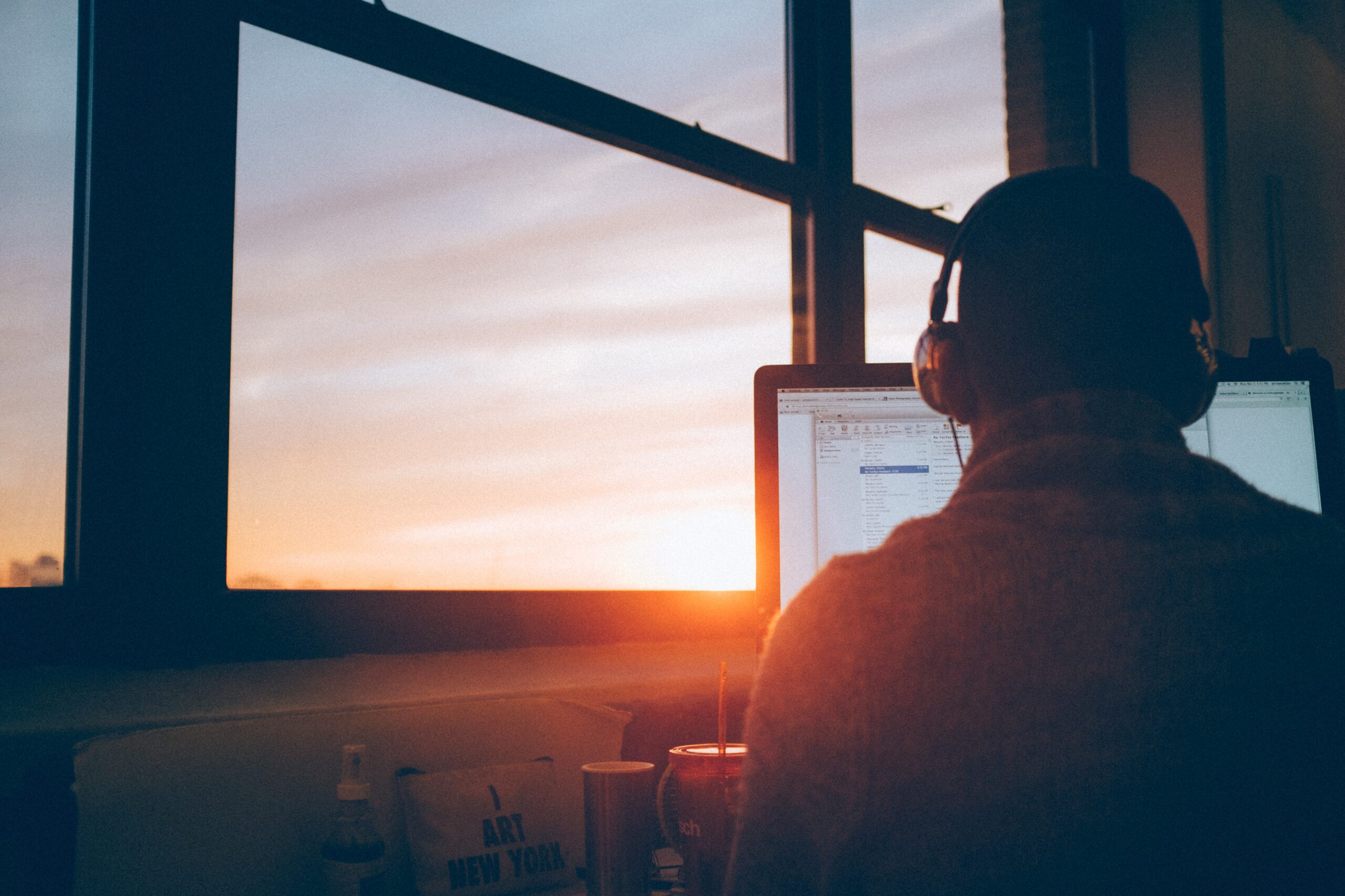 Person with headphones on working on desktop computer at sunset